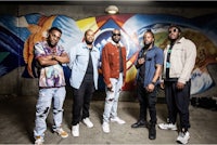 a group of men standing in front of a mural