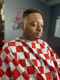 a man in a red and white checkered shirt sitting in a barber shop